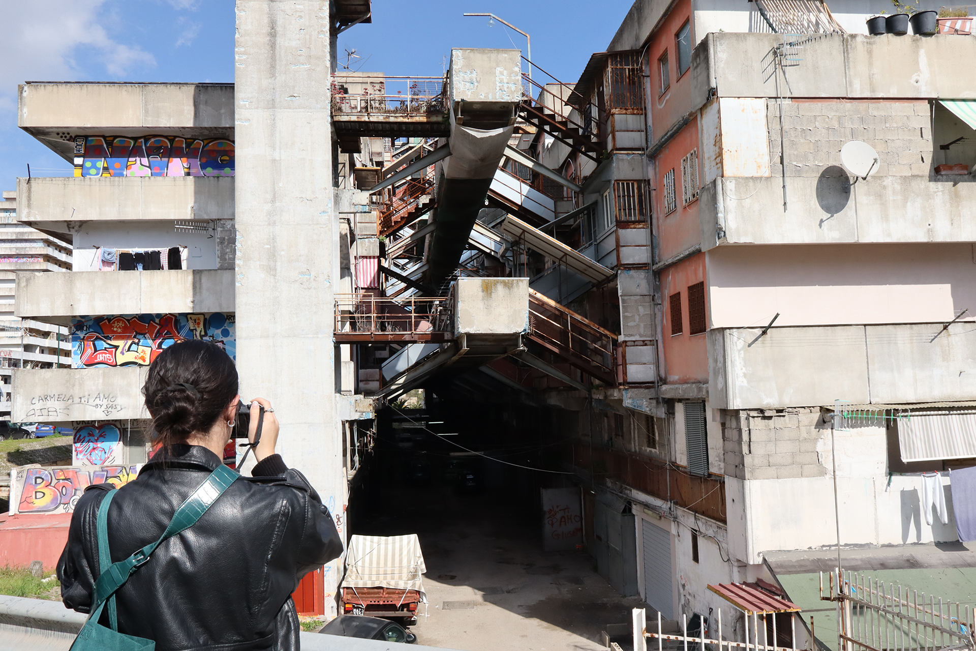 Student in a black jackets takes a picture of a high rise housing project. 