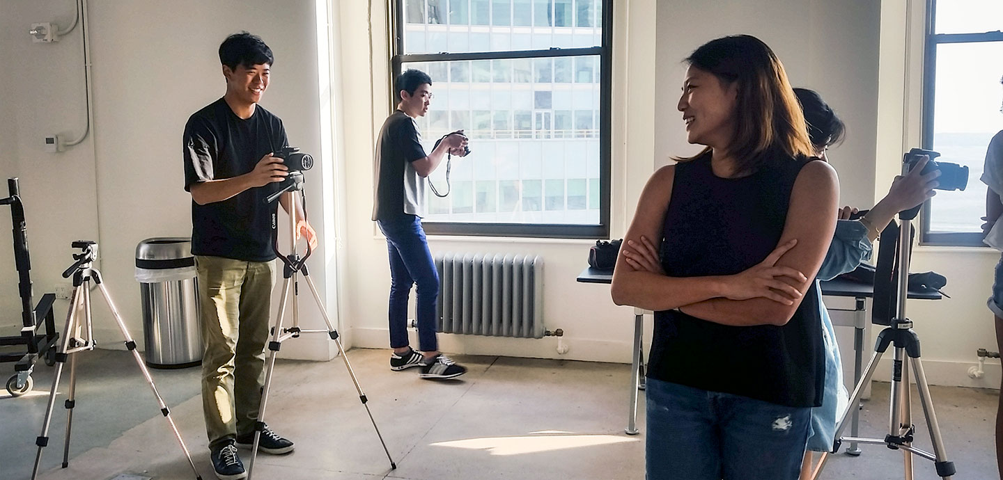 three students with cameras in studio, one student posing for one of the photography students