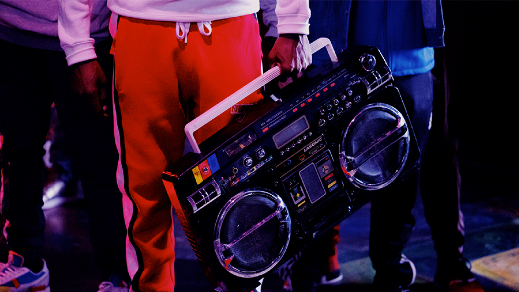 A person holding an old school boom box standing in a group.