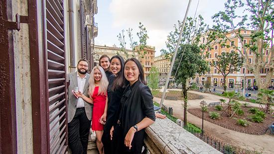 five students standing on a balcony overlooking a street