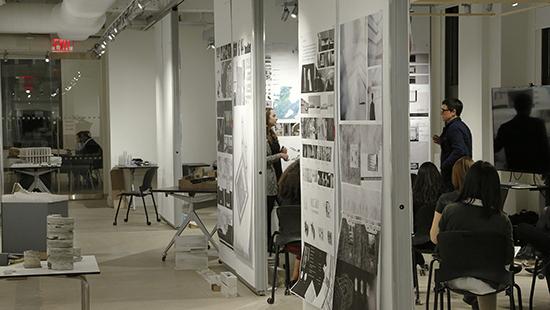 critique of work pinned to movable walls with one faculty and student standing and the other students seated