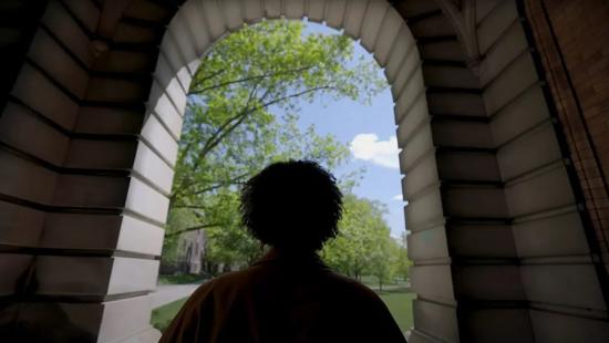 A person standing under a building archway looking out to a field of trees and a blue sky.