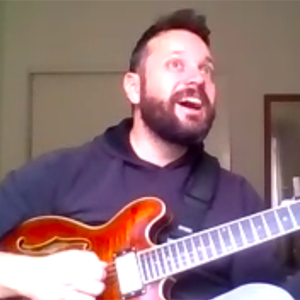 student with short hair and facial hair, blue shirt and guitar