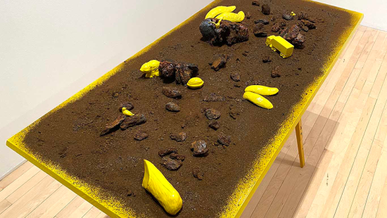 Yellow table with brown dirt, rocks, and yellow figurines spread out on table.