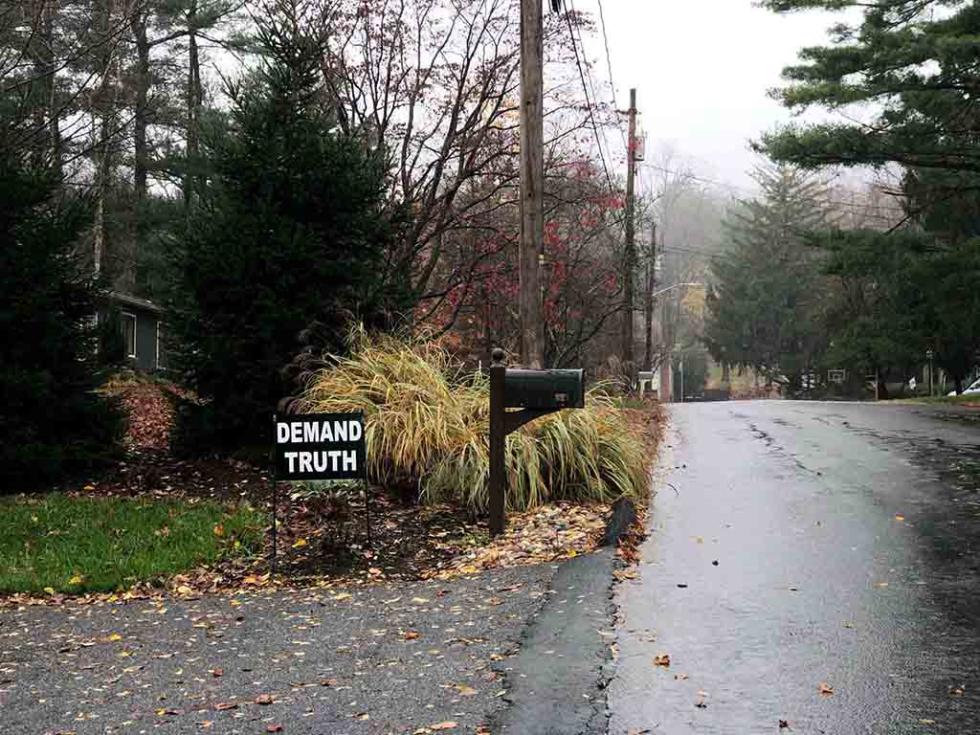 Black and white sign depicting the words DEMAND TRUTH next to a mailbox and on the corner of someone's lawn.