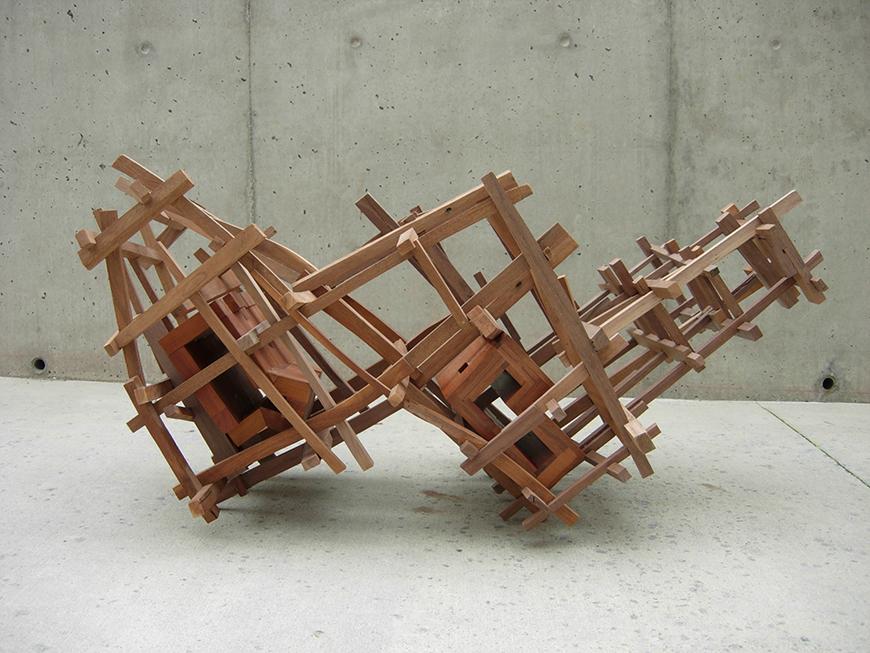 Abstract sculpture piece with wooden pieces attached to one another in a checkered W formation.