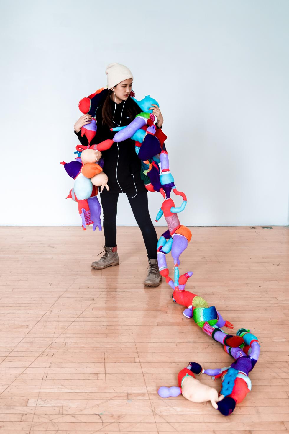 Colorful abstract shapes sewn together, draped across a woman wearing black clothes and gray boots.