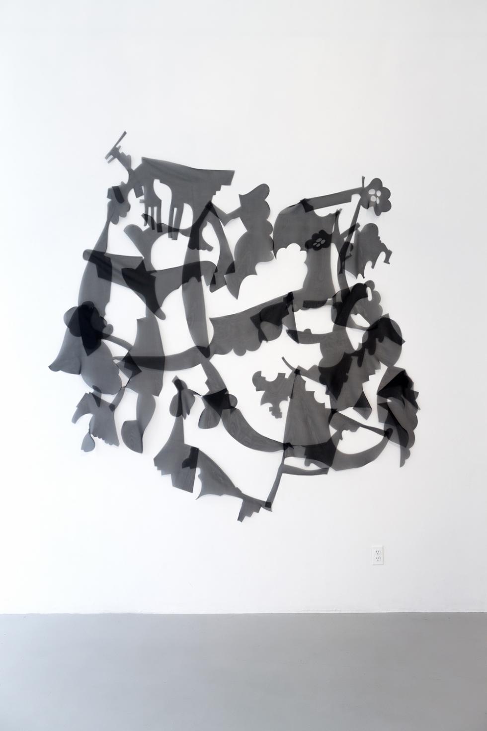 Black and white photo of black transparent abstract shapes against a white wall, with a grey floor. 