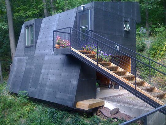 a dark colored metal clad contemporary tiny house with an angled wall and set of stairs on the outside 