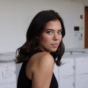 Woman with shoulder length brown hair looking over her shoulder at the viewer.